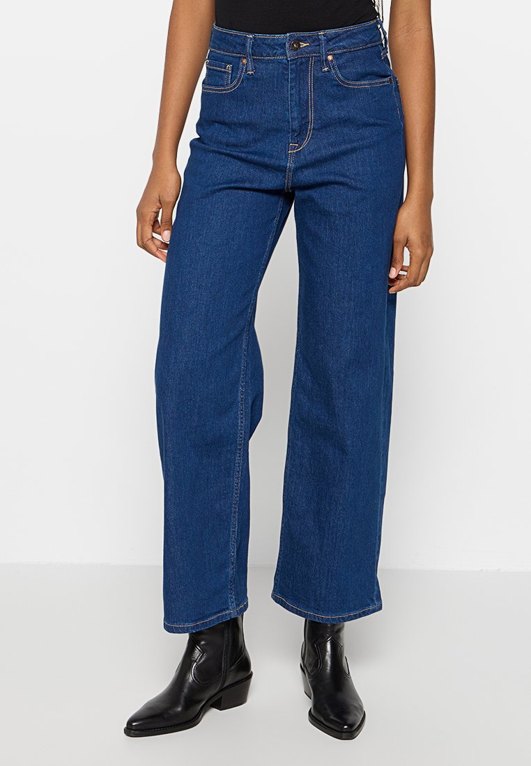 Jeans taille haute à jambes larges en denim bleu foncé avec des coutures orange, dotés d'une fermeture à bouton à l'avant et d'un design classique à cinq poches.