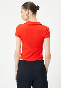 Rød poloshirt med korte ærmer lavet af glat stof. Har en klassisk krave og en cropped pasform, parret med mørkeblå bukser.