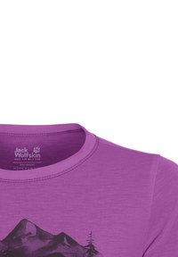 Παιδικό μπλουζάκι Jack Wolfskin σε μωβ χρώμα με μαύρο τυπωμένο γραφικό βουνού και δέντρου στο μπροστινό μέρος.