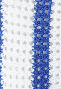 Textil de ganchillo con franjas alternas de color blanco y azul. El material tiene un patrón de tejido abierto y texturizado con un diseño estructurado.