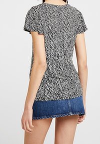 Černobílý patterned top s krátkým rukávem, těsně přiléhající silueta, kulatý výstřih a jemné sklady na ramenech.