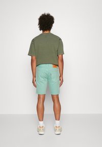 Camiseta de algodón verde, de manga corta, combinada con shorts de denim verde menta. Detalle notable: parche de logo en la cinturilla trasera. Zapatillas blancas.