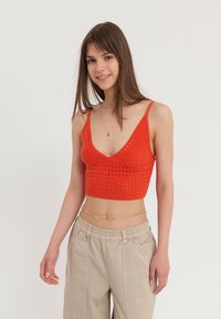 Rød strikket crop topp med dyp V-hals og gittermønster. Kombinert med beige vide bukser og et delikat gullkjede belte.