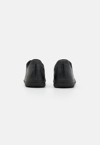 Chaussures noires à enfiler avec surface texturée, présentant des rayures diagonales et une semelle noire flexible. Design minimaliste, sans marque visible.