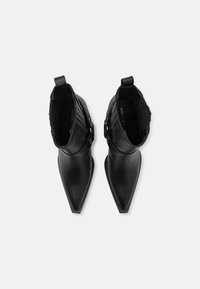 Botas negras hasta el tobillo con punta afilada, material de cuero suave, detalle acanalado en el cuello y acentos de metal.