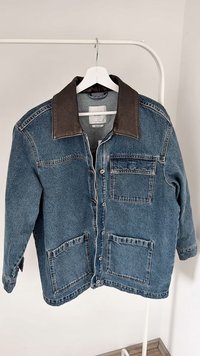Denim jakk, millel on kontrastne pruun nahkhaar, esipidamad, nööbiga sulgemine ja lõdvestunud mugavus. Heledat sinist värvi koos tekstuuriga kangaga.