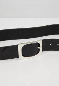Cinturón de cuero negro con una hebilla rectangular de plata, textura suave y múltiples agujeros para ajustar el tamaño. Diseño sencillo y funcional.