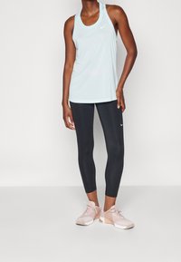 Valko sininen ilman hihoja oleva urheilupaita, mustat tiukat legginsit ja vaaleanpunaiset urheilukengät verkkoyksityiskohdilla. Nike-logo paidassa ja kengissä.
