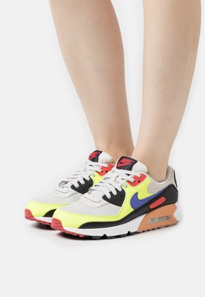 Tenisky Nike Air Max v šedé, žluté a černé barvě s modrými a červenými akcenty. S texturovanou síťovinou, polstrovaným jazykem a viditelným vzduchovým odpružením.