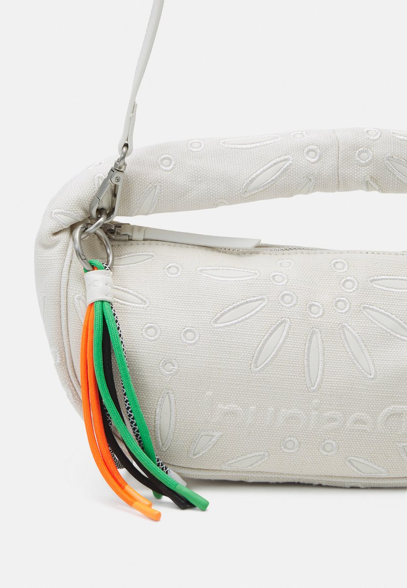 Bolso de tela blanca con un patrón de hojas en relieve, que presenta un asa curva y borlas decorativas multicolores en naranja, verde, negro y gris.