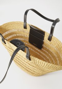 Kudottu olkakassi heinistä, jossa on leveä aukko, mustat nahkahännät ja sisäinen nahkatasku. Luonnollinen väri, jossa on teksturoitu pinta.