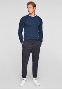 Marineblauer Strickpullover mit gerippter Textur und Rundhalsausschnitt, kombiniert mit dunklen Jogginghosen, die einen elastischen Bund und schmal zulaufende Bündchen besitzen.