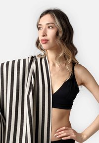 Shawl a righe bianche e nere realizzato in tessuto morbido, drappeggiato su una spalla. Modella che indossa un reggiseno sportivo nero, design minimalista, texture liscia.