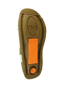 Suela de zapato con material de goma texturizado marrón. Presenta una etiqueta naranja con información sobre sostenibilidad y un logotipo. Forma redondeada con surcos.