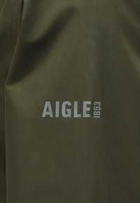 Tissu vert avec un texte gris clair disant "AIGLE 1853" imprimé dessus.