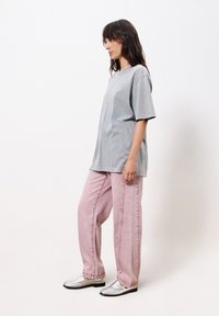 Graues, übergroßes T-Shirt, rosa lockere Jeans und silberne Loafers. Das Outfit zeichnet sich durch ein schlichtes Design und leichte Texturen aus.