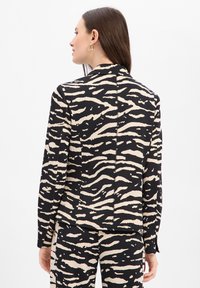 Zwart-beige blazer met zebraprint, een getailleerde pasvorm, lange mouwen en een gladde textuur. De achterkant heeft een centraal stiksel als detail.