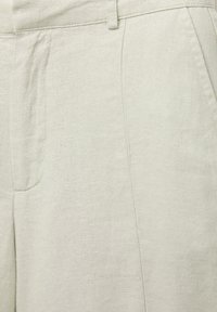 Jasnozielone lniane spodnie o gładkiej fakturze, z dopasowaną talią, bocznymi kieszeniami i subtelnymi zakładkami dla efektu dopasowanego kroju.