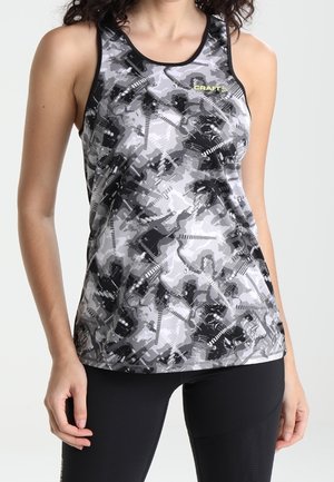 Mujer vistiendo una camiseta deportiva sin mangas con patrón abstracto de camuflaje en gris, negro y blanco con el logo "CRAFT", combinada con leggings negros.