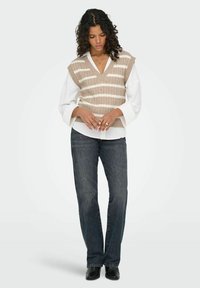 Neuleliivi, jossa on pystysuunnassa vaaleanbeigejä ja valkoisia raitoja, kerroksittain valkoisen napillisen paidan päälle. Tummat farkut ja mustat saappaat viimeistelevät asun.