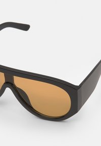 Ochelari de soare negri, de mari dimensiuni, cu un design elegant și unghiular și lentile de culoare maro. Construiți din plastic neted, cu detalii hardware minime.