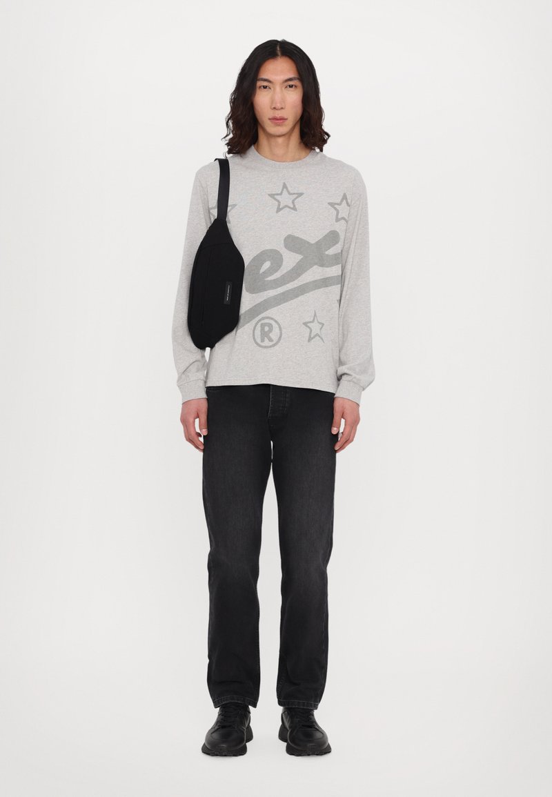 Gray long-sleeve shirt with star pattern and logo, paired with black jeans and black sneakers. The shirt has a relaxed fit and crew neck.