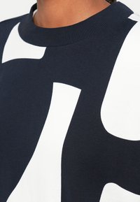 Sudadera azul marino con grandes formas abstractas blancas, cuello de canalé, textura suave y mangas cortas. Enfoque en el patrón geométrico.