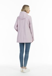 Lichtroze waterdichte jas met capuchon, lange mouwen en een rechte snit, gecombineerd met blauwe skinny jeans en witte sneakers.