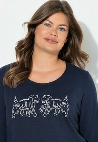 Maglietta a maniche lunghe color blu navy con grafica contornata bianca di due cani che si fronteggiano. Tessuto morbido con scollo rotondo e vestibilità comoda.