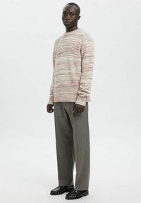 Maglione color beige chiaro con strisce rosate, trama lavorata a maglia, scollo rotondo e polsini a costine, abbinato a pantaloni grigi a gamba larga e scarpe nere.