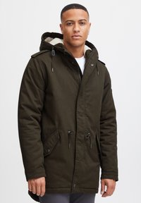 Mörkgrön parka-jacka med dragkedja och tryckknappar fram, justerbara dragsnören och ett mjukt beiget foder i huvan, med sidofickor.