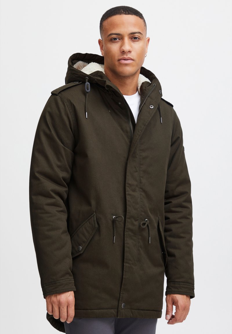 Mörkgrön parka-jacka med dragkedja och tryckknappar fram, justerbara dragsnören och ett mjukt beiget foder i huvan, med sidofickor.
