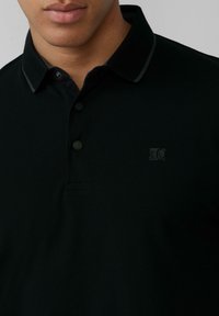 Czarna koszulka polo z teksturowanej tkaniny, trzy guziki i małe logo na lewej piersi. Posiada kontrastowy wykończenie kołnierzyka.