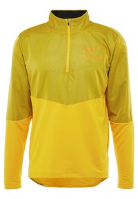 Sudadera deportiva amarilla con cremallera de cuarto, con parte superior texturizada y sección inferior suave, que presenta un logo naranja y mangas largas.