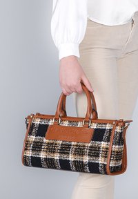Handväska med en rutigt svart, vitt och brunt tyg som kropp, kompletterad med läderdetaljer i tan och en framträdande logopanel.