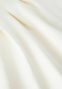 Tissu couleur crème avec une texture lisse, présentant de doux plis et un léger éclat, disposé de manière fluide et drapée.