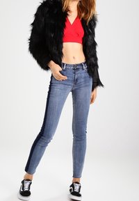 Černá kabát z umělé kožešiny, červený zkrácený top, světle modré úzké džíny se stranovými pruhy a černé tenisky s bílou podrážkou.