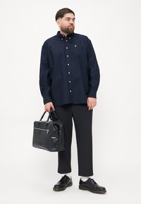 Navy button-up shirt with a chest pocket and logo, paired with loose black trousers, black shoes, and a textured black handbag.