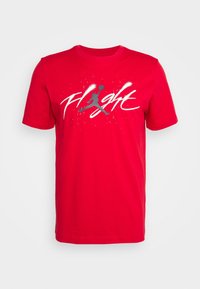 Punainen lyhythihainen T-paita, joka on valmistettu puuvillasta. Siinä on valkoisena ja harmaana "Flight" -grafiikka, jossa on koripalloilijan siluetti.