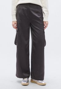 Voľné nohavice s cargo vreckami z tmavohnedého saténu. Majú bočné vrecká, hladkú textúru a strihaný strih. Kombinované so striebornými teniskami.