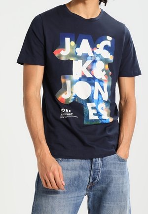 T-shirt bleu marine avec un imprimé graphique multicolore affichant "JACK & JONES" en texte audacieux et superposé. Manches courtes et col rond.
