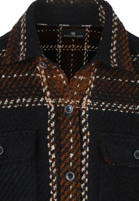 Zwarte en bruine geruite shirt met een wolachtige textuur, knopen aan de voorkant, borstzak en contrasterende patronen in warme tinten.