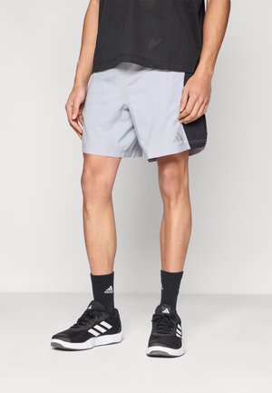 Pantaloncini sportivi grigi con pannelli in rete, dotati di una vita elastica e un dettaglio nero. Abbinati a scarpe da ginnastica e calzini neri.