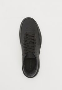 Μαύρο αθλητικό παπούτσι από δέρμα με κορδόνια, τρυπητό σχέδιο στην μύτη και πράσινο λογότυπο Lacoste στην περιοχή της φτέρνας, �εμφανιζόμενο από άποψη κορυφής σε λευκό φόντο.