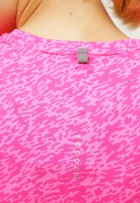 Camiseta atlética rosa con un patrón texturizado, detalle en la parte posterior con una etiqueta gris y pequeños acentos blancos a lo largo del borde inferior.