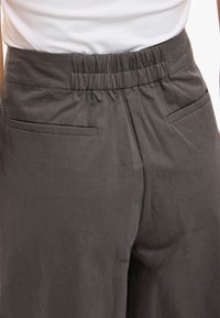 Tummanharmaat housut, joissa joustava vyötärönauha, kaksi etutaskua, sileä pinta ja suora lahjemalli. Saumat ovat siististi viimeistelty.