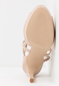 Beige hoge hak sandaal met dunne enkelbandjes, puntige neus en een gestructureerde rubberen zool. Heeft een minimaal ontwerp en een smalle hak.