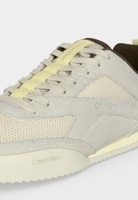 Μπεζ και ανοιχτό κίτρινο sneaker Calvin Klein με υφή από δίχτυ, επενδύσεις από σουέντ, κρεμάλια σόλας και υφασμάτινα κορδόνια περασμένα μέσα από θηλιές.
