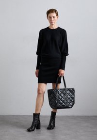 Pulover negru tricotat, fustă cu cuta și geantă neagră matlasată. Botine din piele, de înălțime ankle, cu toc pătrat. Textura materialului este netedă.