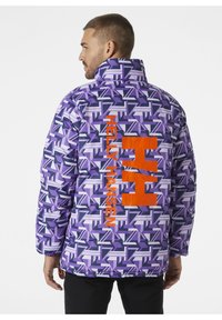 Chaqueta de color púrpura con un patrón que presenta una mezcla de formas geométricas, con un logo naranja "HH" y el texto "HELLY HANSEN" en la parte posterior.